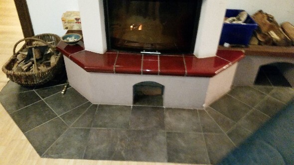 Kamin mit rotem Fliesenrand im Wohnzimmer, dunkle Bodenfliesen und Körbe daneben.