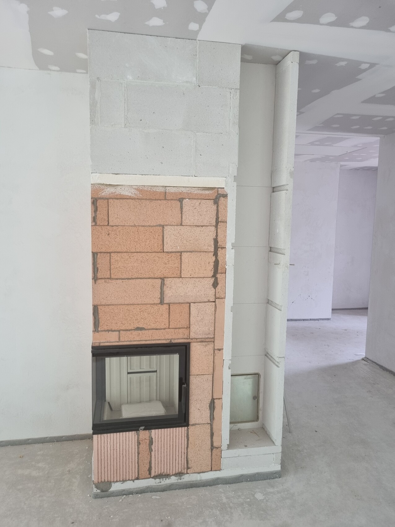 Kamin aus rotem Ziegel in unfertigem Innenraum, Sichtfenster, Rohbau-Decke.