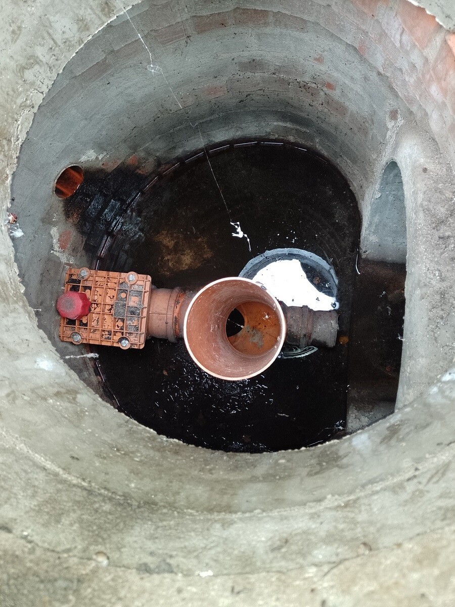 Offener Beton-Schacht mit großem Kupferrohranschluss und Ventilantrieb im Wasser.