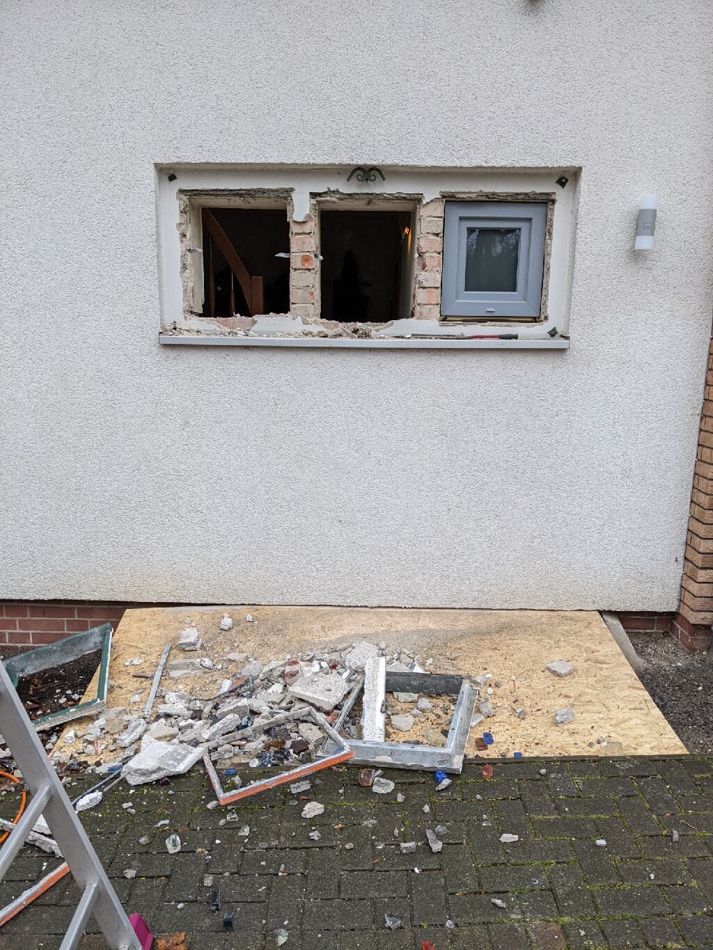 Beschädigte Außenwand mit offener Fensternische, Baugerümpel und Bruchstücke davor.