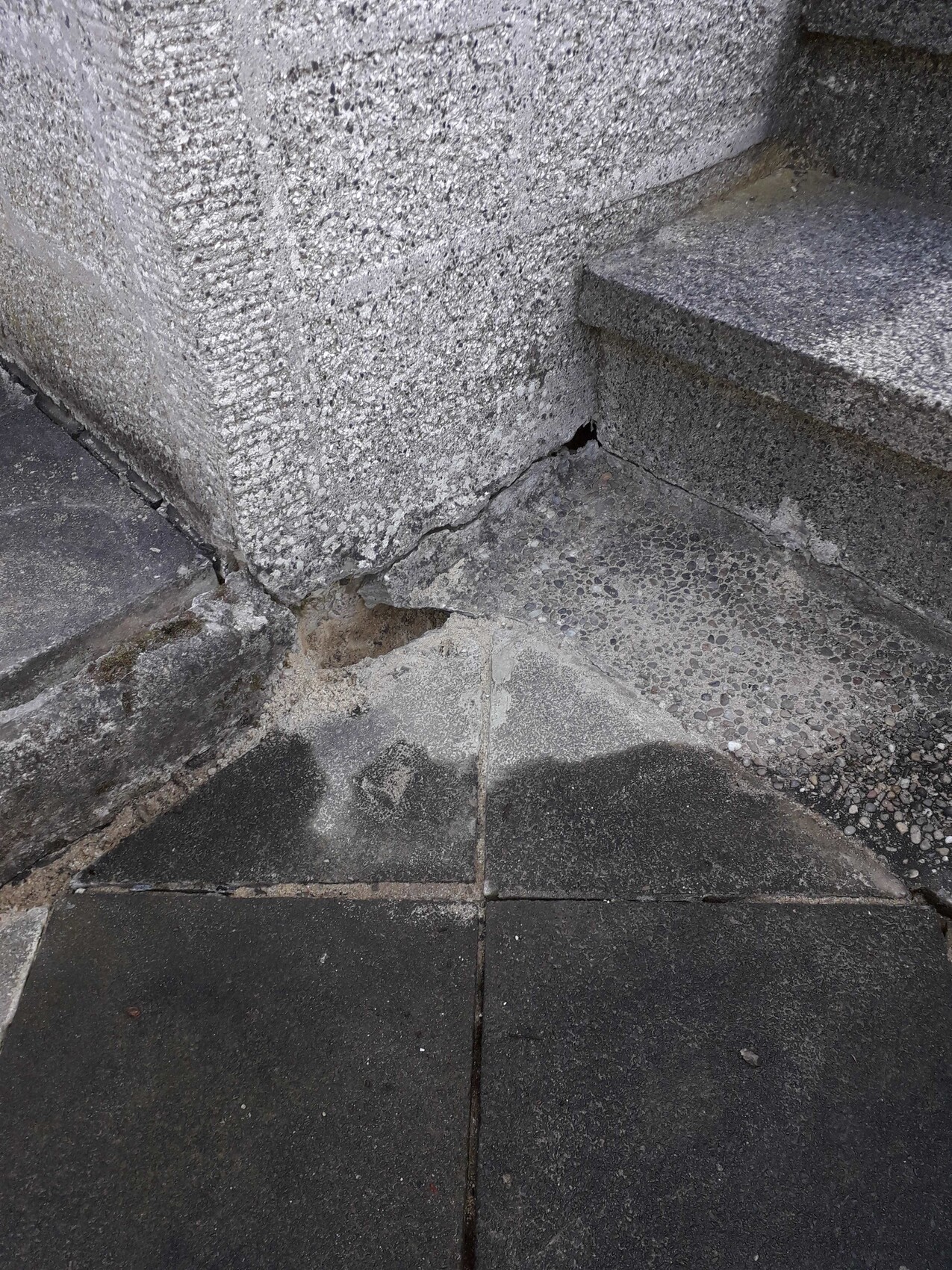 Betonte Ecke mit Treppenstufen rechts, Wand mit Riss und feuchtem, dunklem Boden.