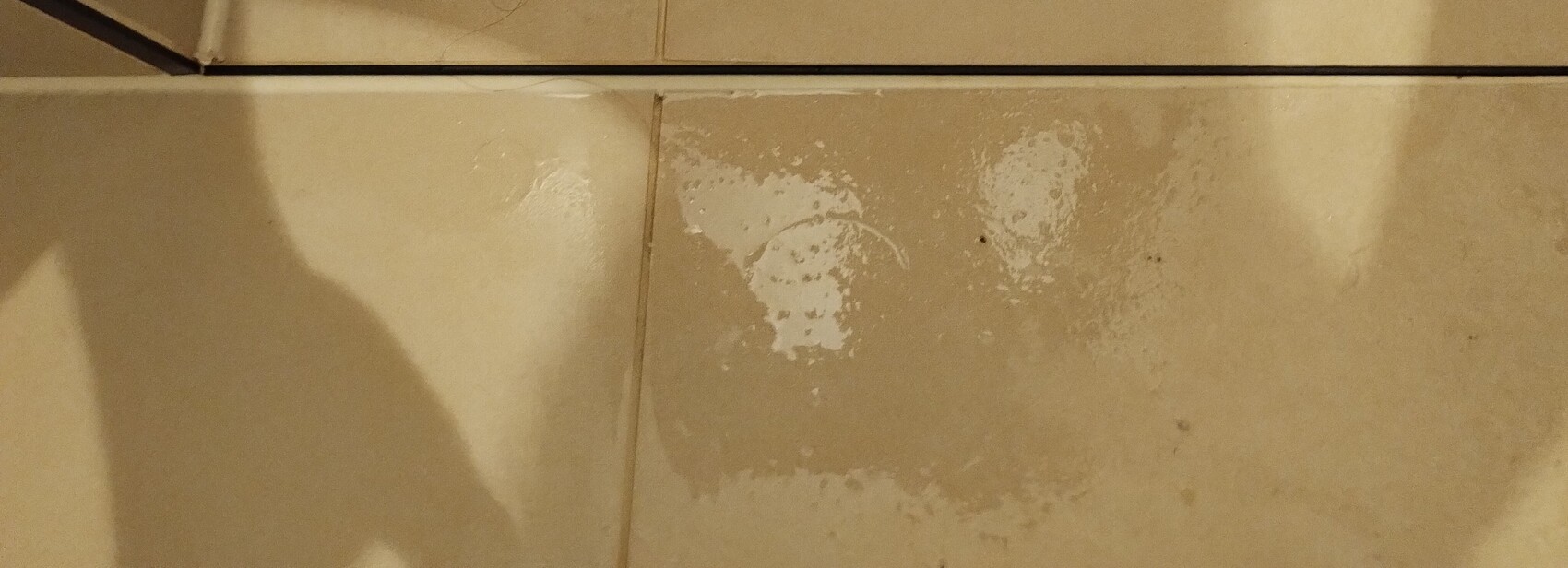 Beige Fliesenboden mit Schatten links und weißen Flecken auf einer Fliese.