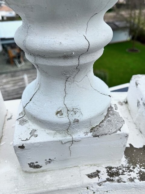 Weiße Außenbalustrade mit Rissen und Abplatzungen am Sockel.