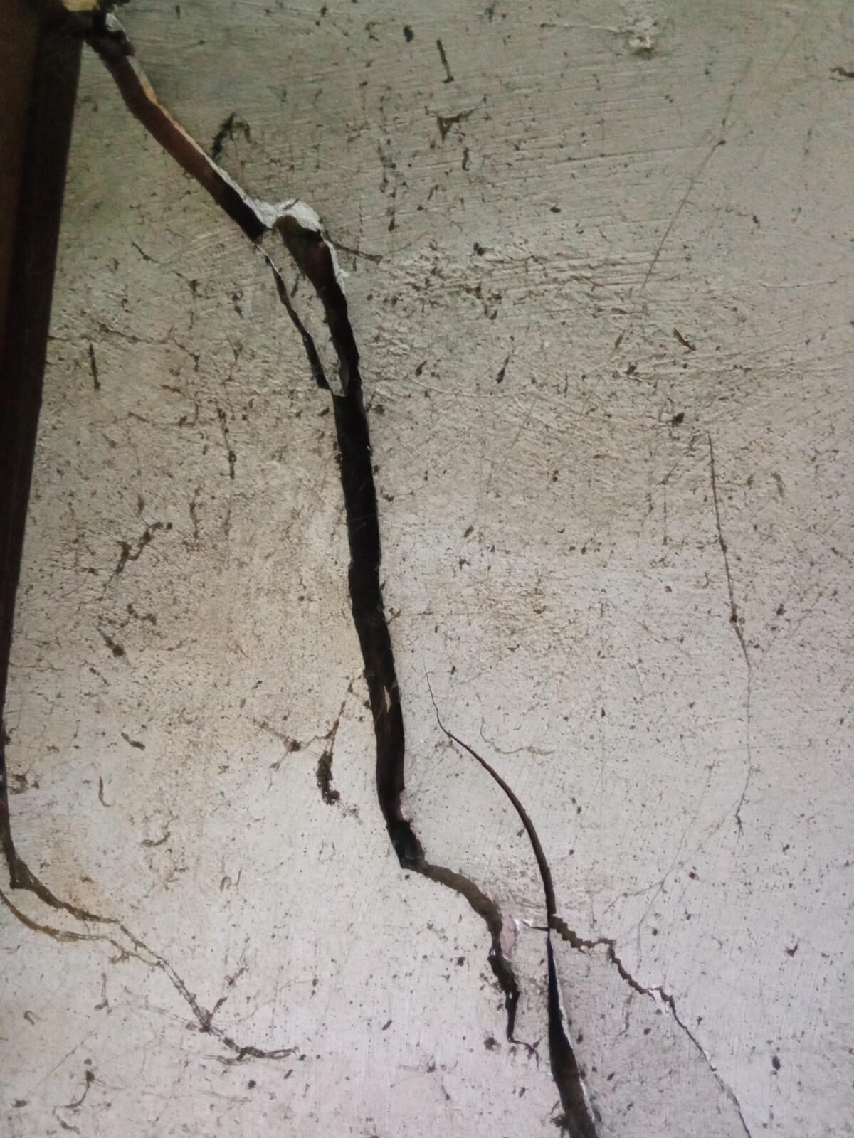Rissige Verputzwand mit langem vertikalen Spalt und bröckelndem Putz.