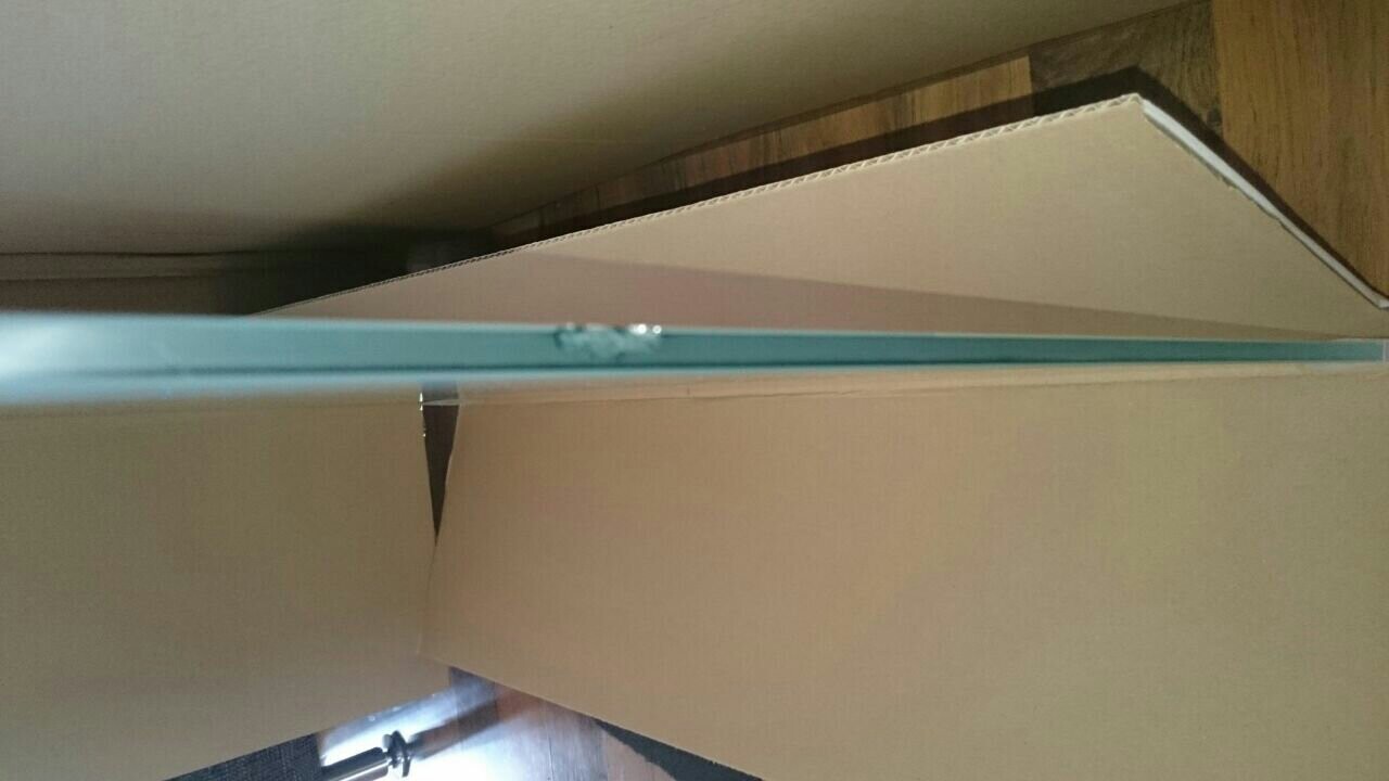 Eine seitlich stehende Kartonverpackung in einem Wohnraum neben Holzboden.