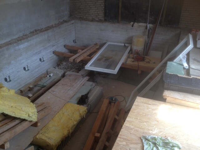 Baustelle im Keller mit Fensterrahmen, Dämmmaterial und Holzplanken