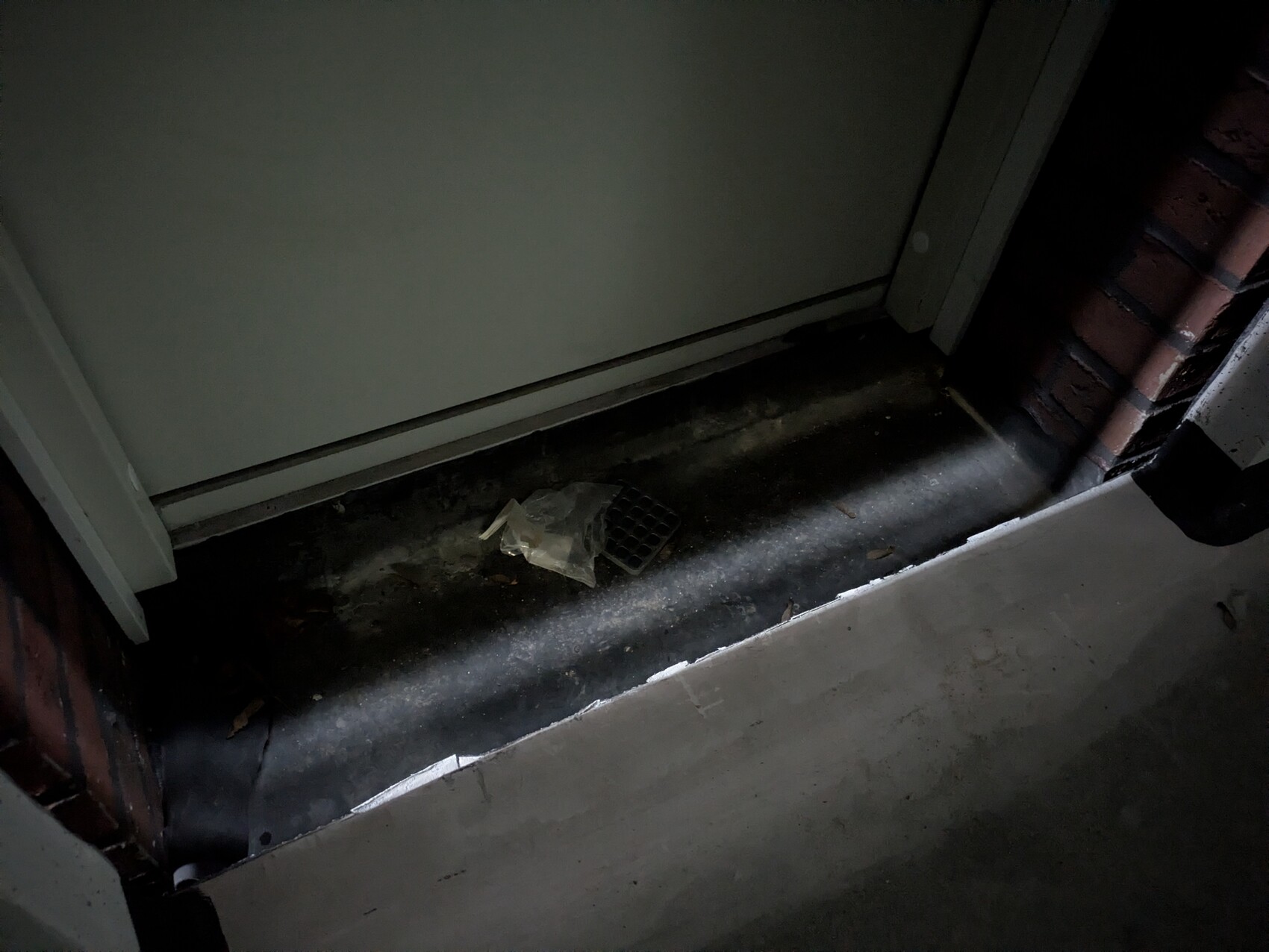 Kellerboden mit Bodenablauf, dunkler Kellergang, Türrahmen und Backsteinwand