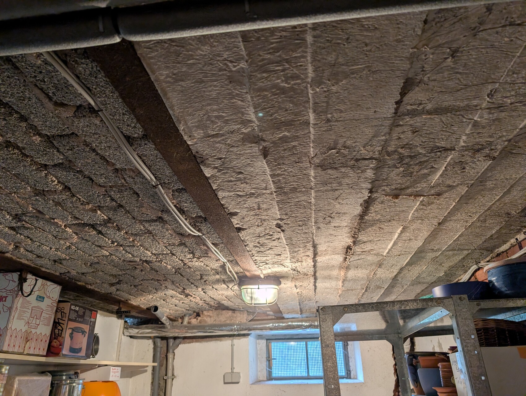 Kellerdecke mit Dämmung, sichtbare Kabel, Leiter und Baumaterial im Kellerraum