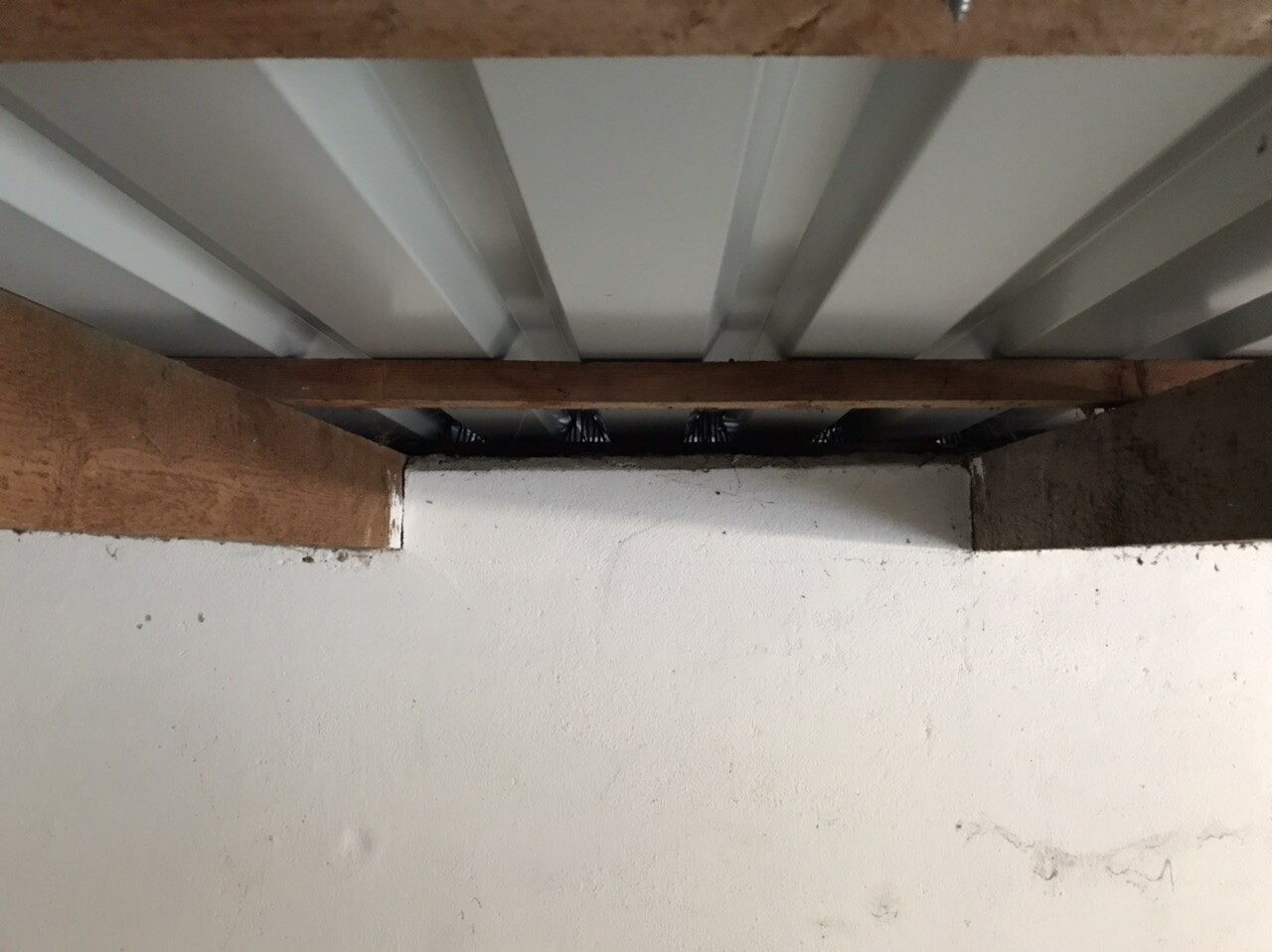 Unterseite einer Kellerdecke: Holzbalken, Stahlträger, dunkler Spalt zwischen Strukturen.