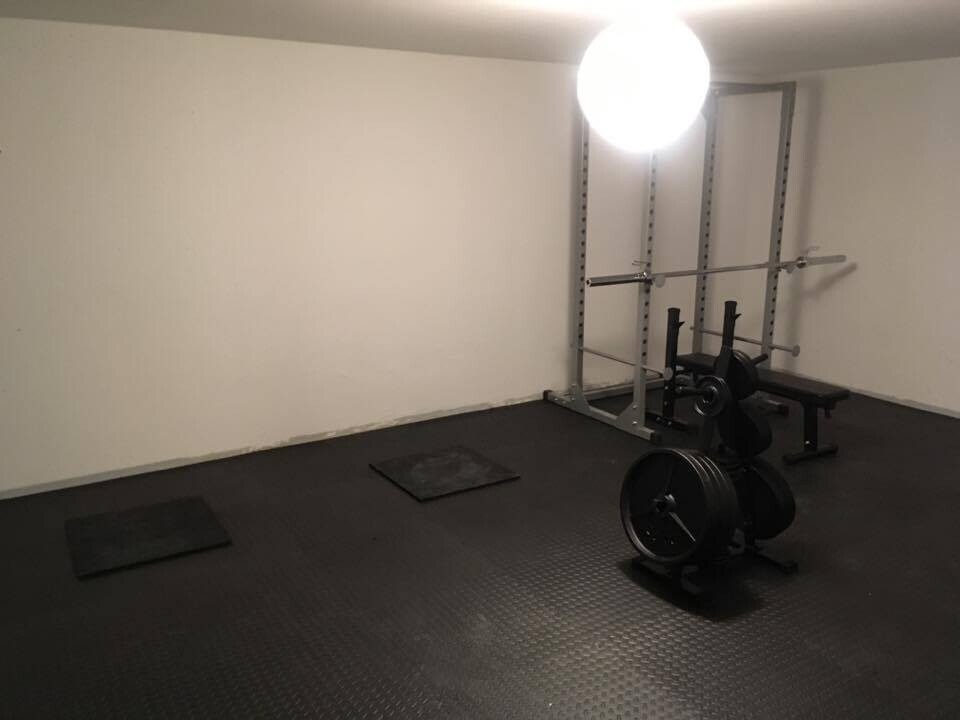 Kleines Heim-Fitnessstudio mit Langhantel, Squat-Rack, Hantelbank und Gewichtsplatten.