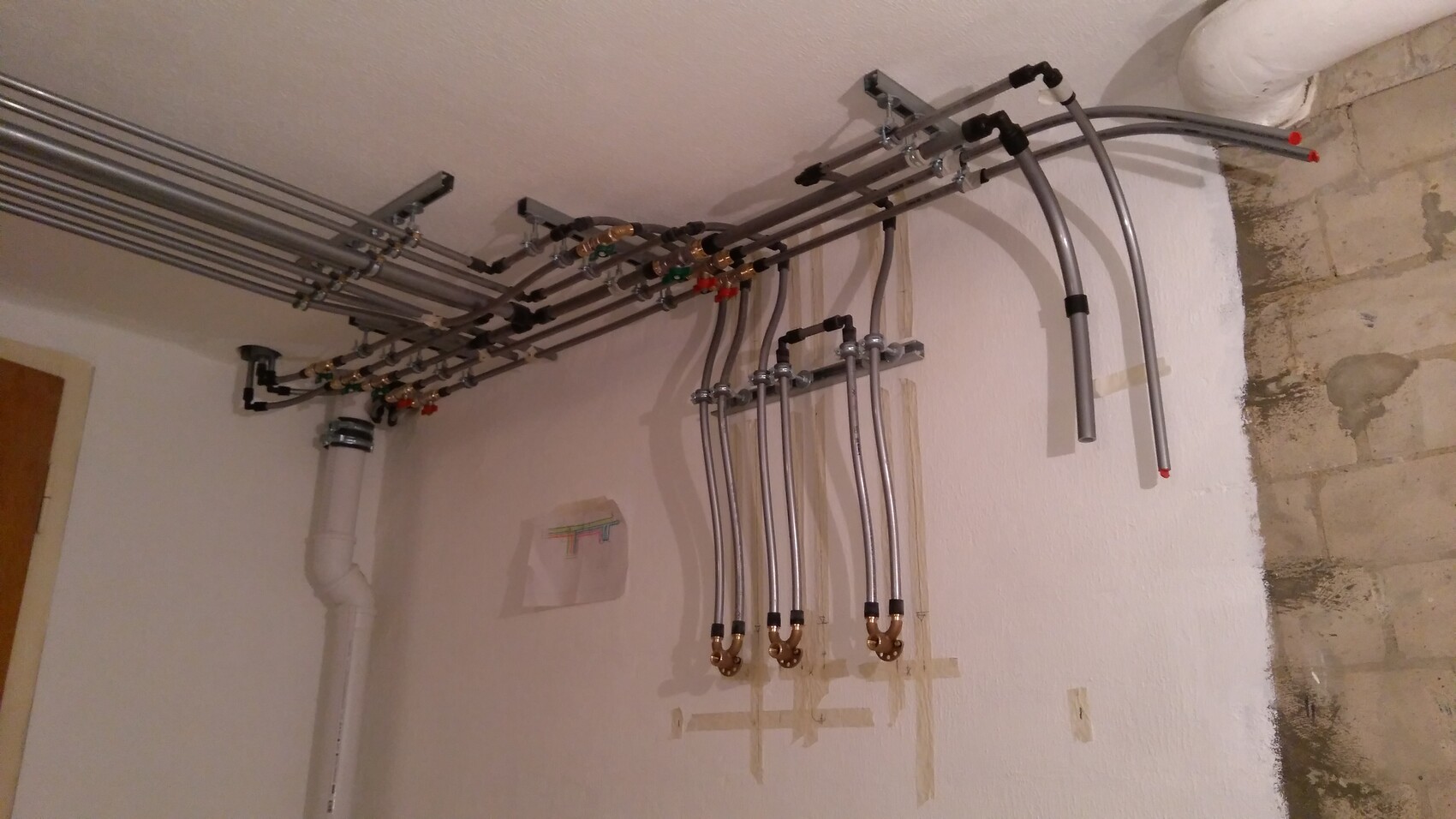 Ansammlung von Metallrohren, Ventilen und Anschlüssen an einer Wand eines Technikraums.
