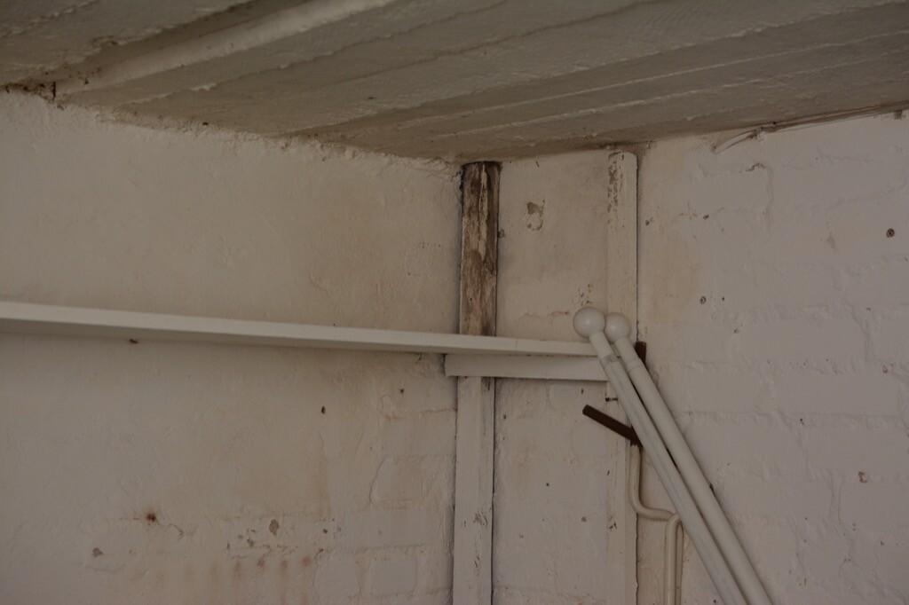 Kellerwand mit weißen Rohren, Kabeln und Holzbalken im Rohbau