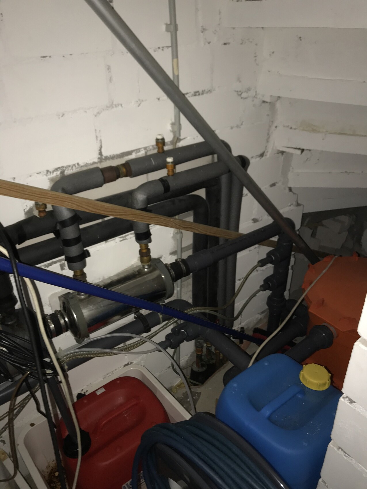 Kellerinstallationsraum mit Rohren, Ventilen, Pumpe, Kabeln und blauem Kanister.