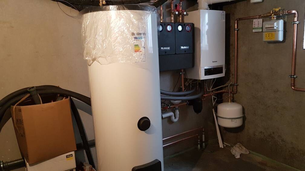 Heizungsraum mit Warmwasserspeicher, Ausdehnungsgefäß, Kupferrohren und Messgeräten.