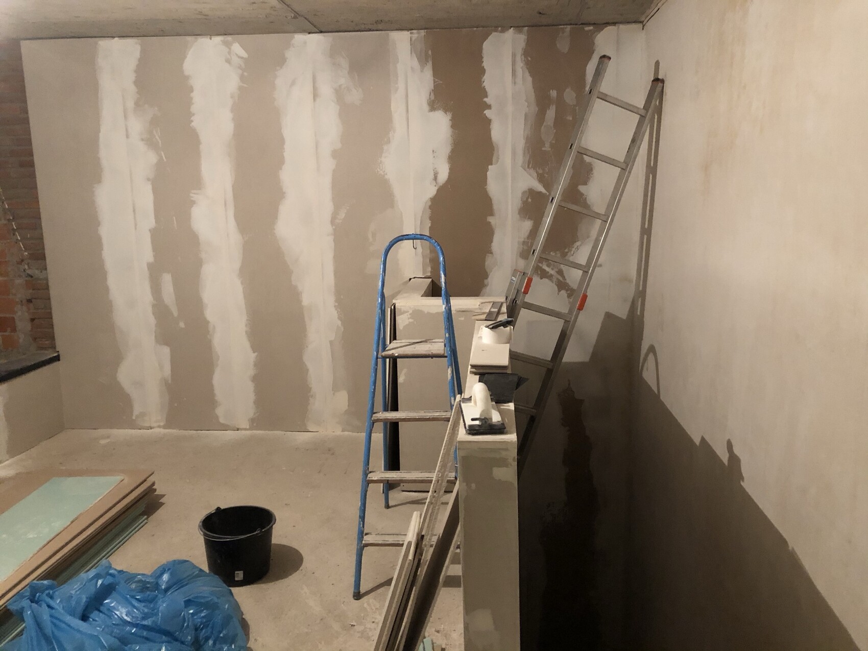 Kellerraum im Bau: ungespachtelte Trockenbauwand, zwei Leitern, Baumaterialien und Eimer.