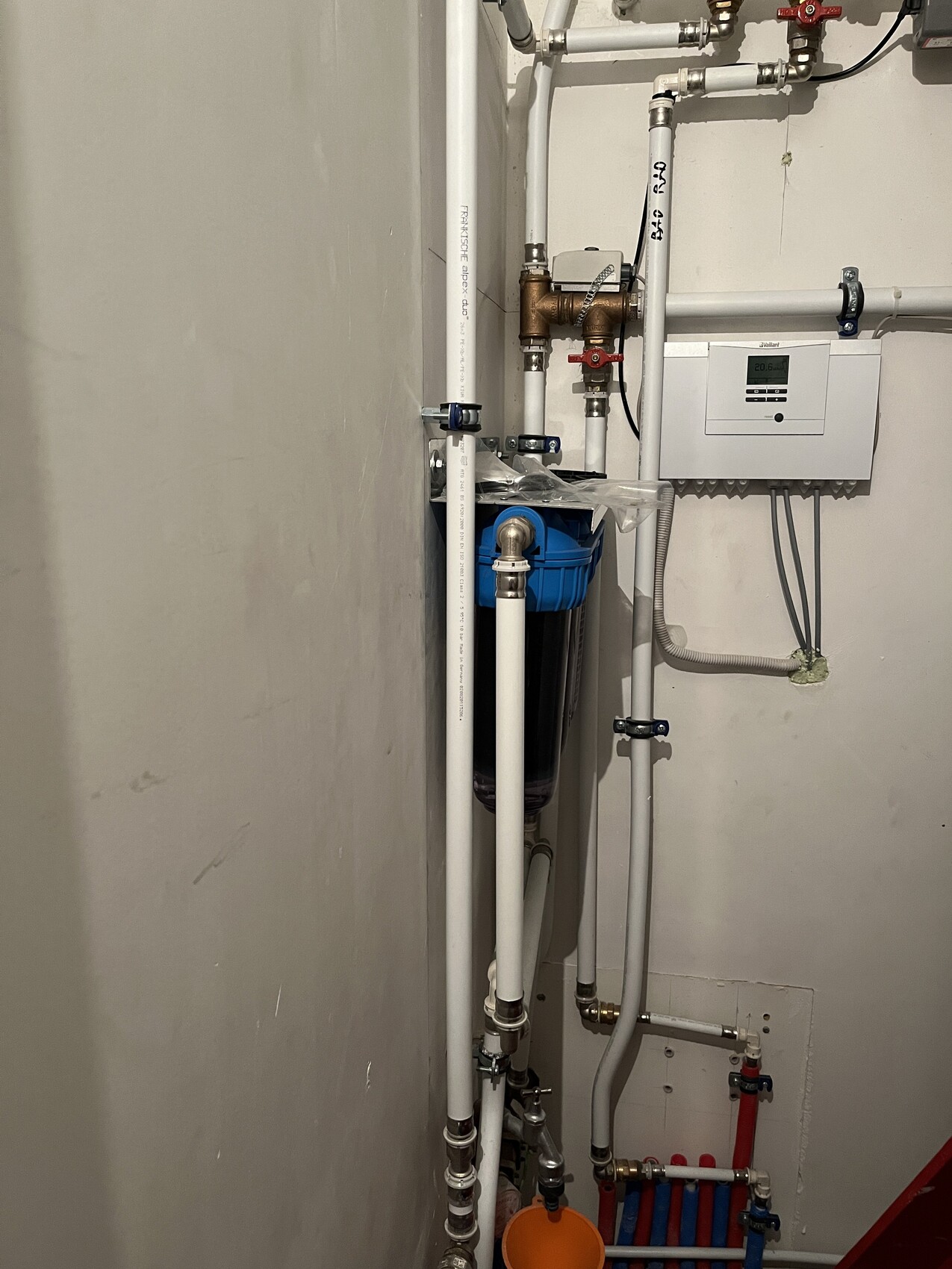 Installationsraum mit vielen weißen PVC-Rohren, roten Ventilen, blauem Wasserfilter und Steuergerät.