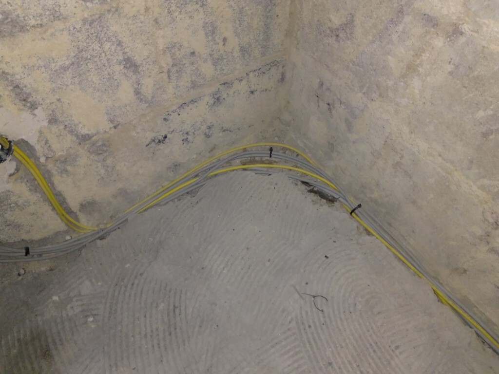 Eckwinkel eines rauen Betonraums mit gelben Kabeln, die am Boden und entlang der Wand verlegt sind.