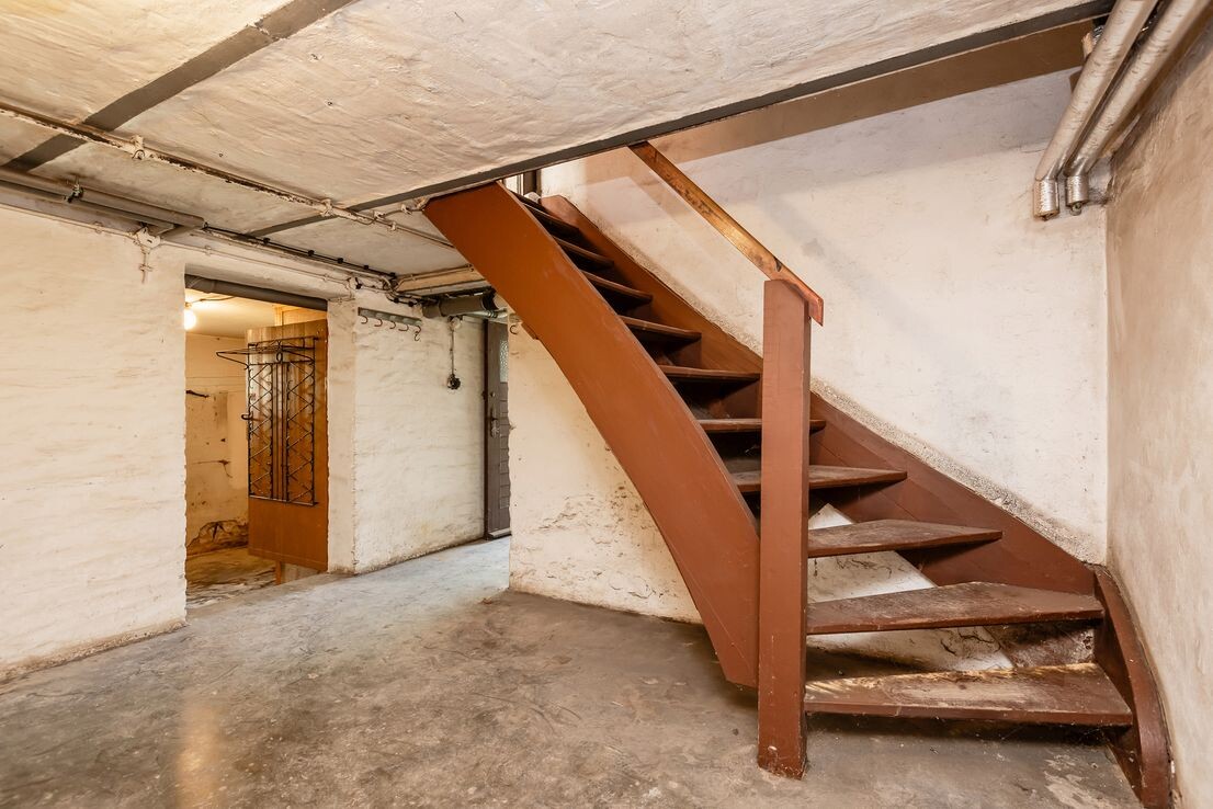 Kellerraum mit roter kurviger Metalltreppe, rauen Wänden und Betonboden