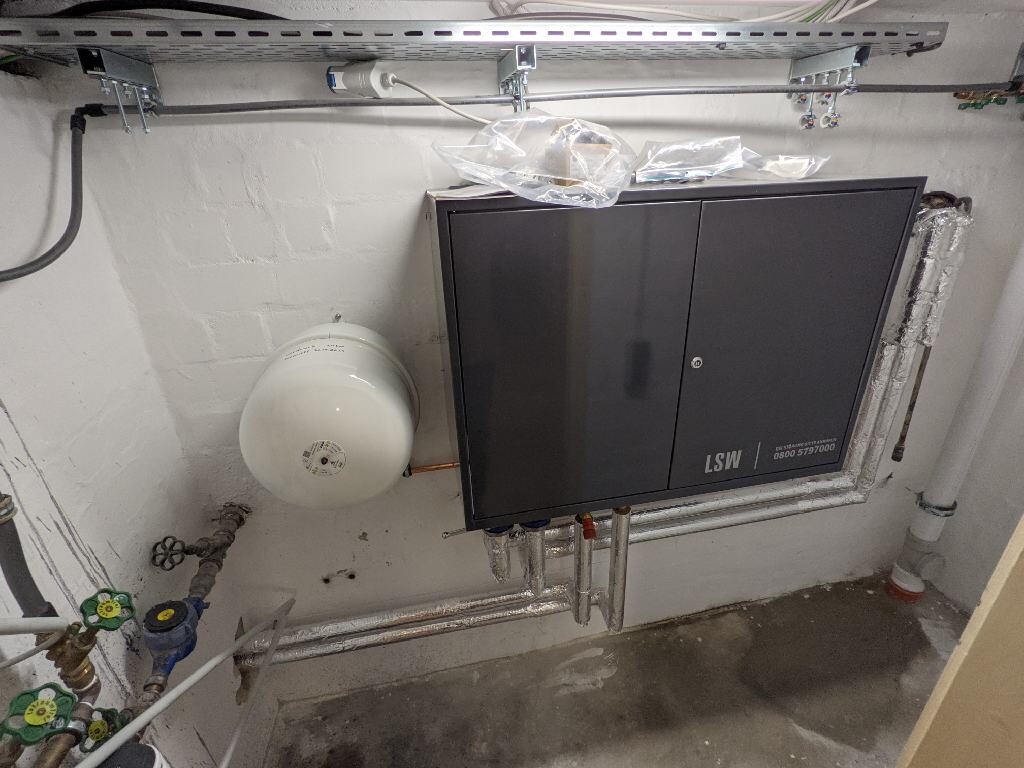 Grauer Installationsschrank mit Rohren und Ausdehnungsbehälter im Keller