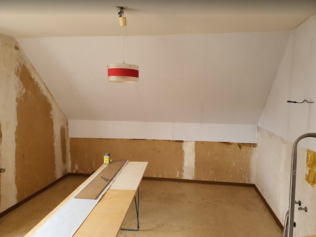 Renovierungsraum im Dachgeschoss mit roter Pendelleuchte, Brettern auf einem Tisch.