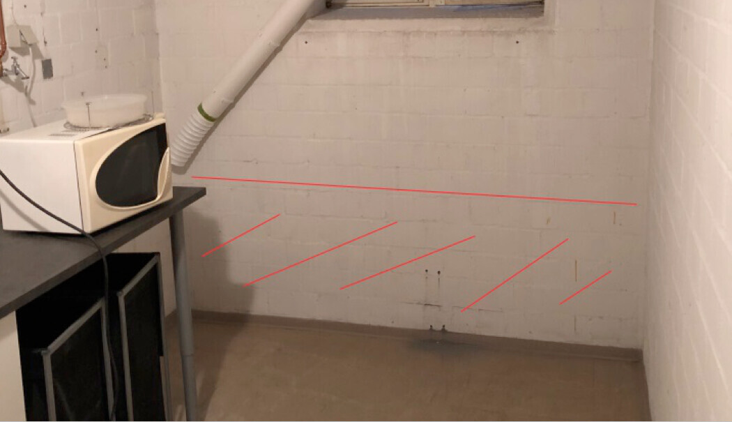 Kellerraum mit Mikrowelle auf einer Arbeitsfläche, weißen Ziegelwänden und roten Markierungslinien an der Wand.