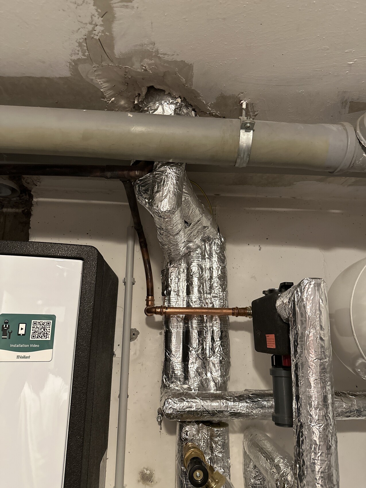 Heizungsanlage mit isolierten Rohren, Kupferleitungen und silberner Dämmung; Vaillant-Gerät sichtbar.