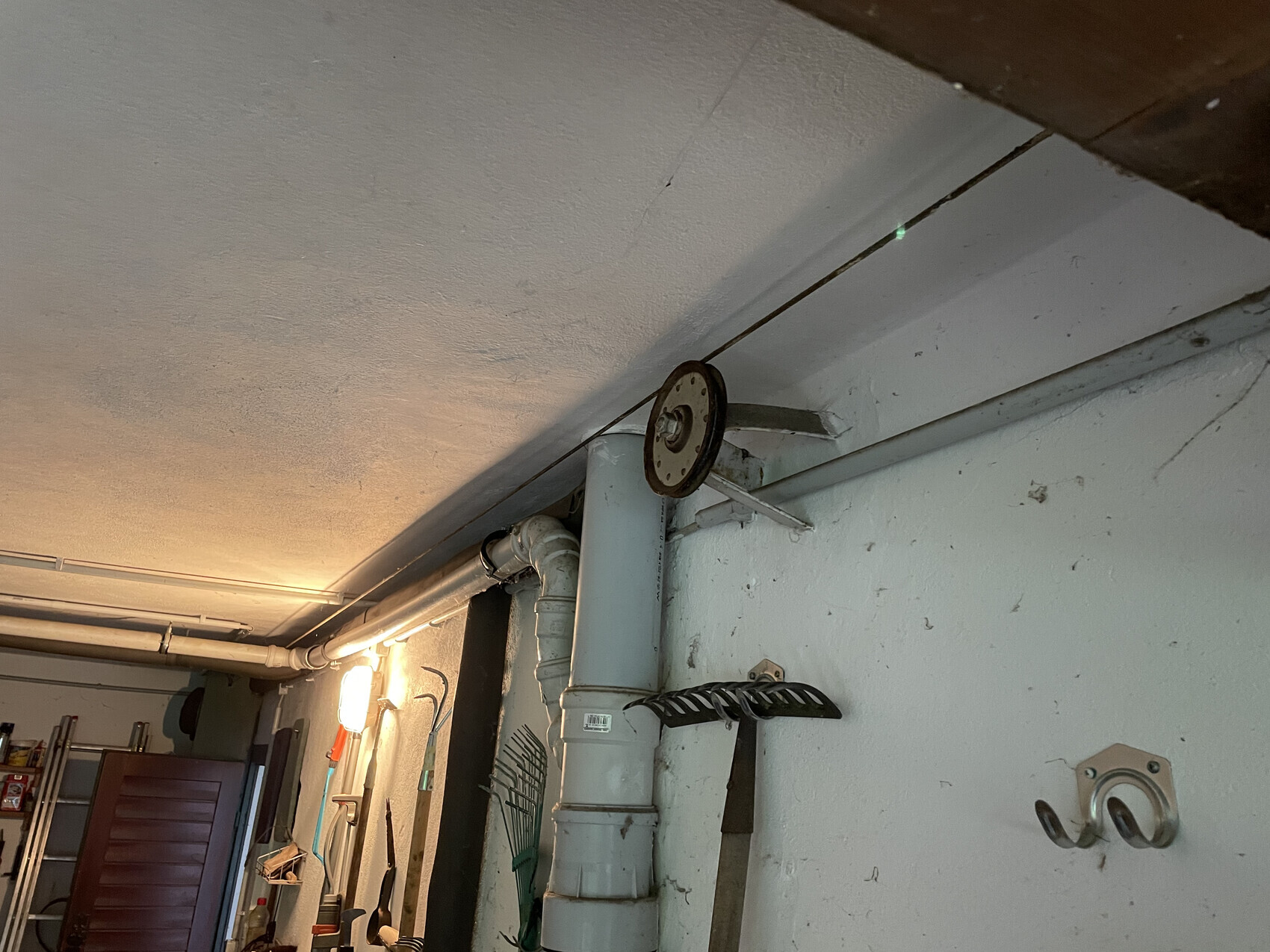 Keller/Waschküche mit Rohren, PVC-Abfluss, rundem Wandrad und Haken.