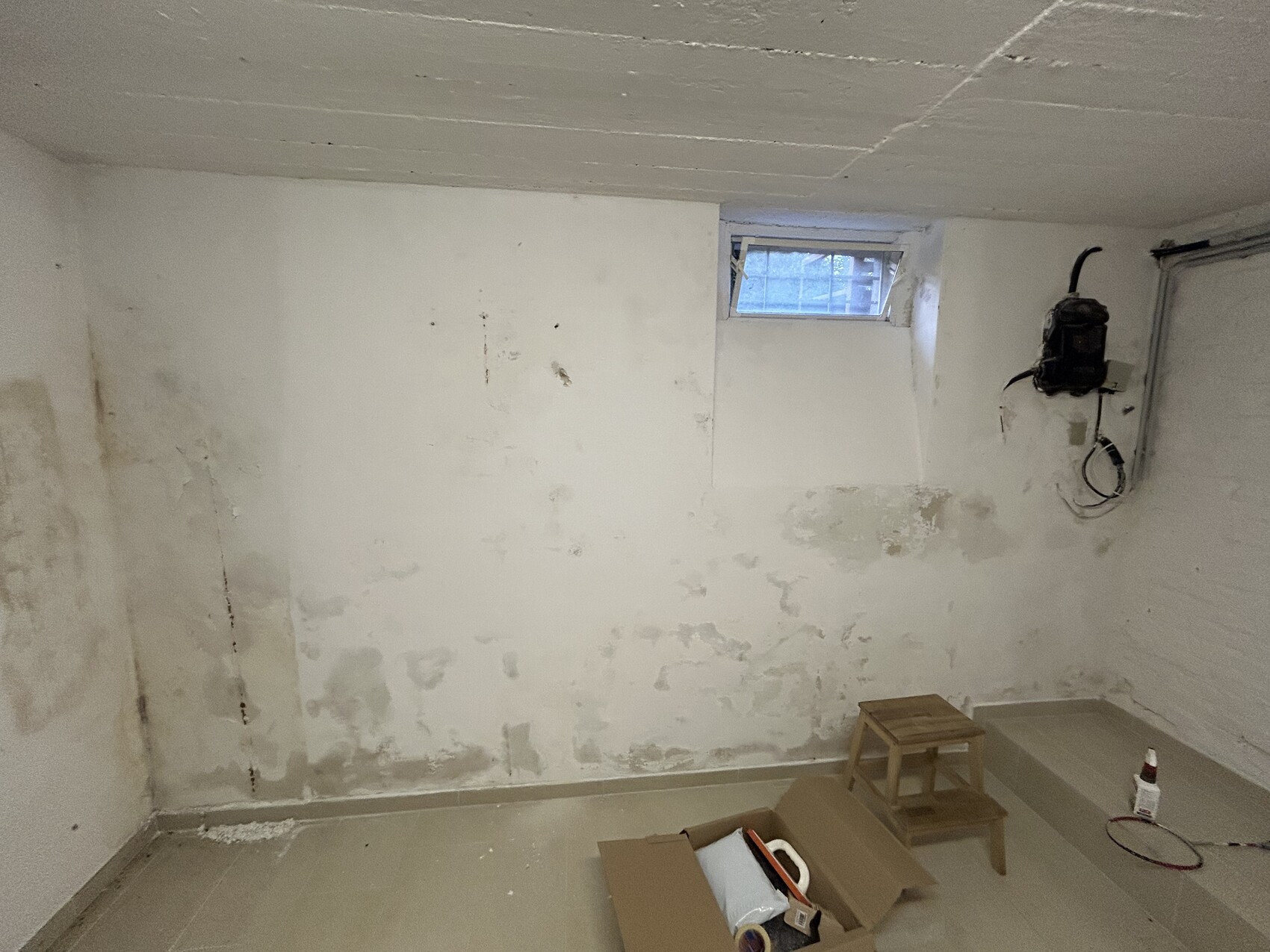 Kellerraum mit rauen, ungestrichenen Wänden, kleinem Fenster und Bauwerkzeugen