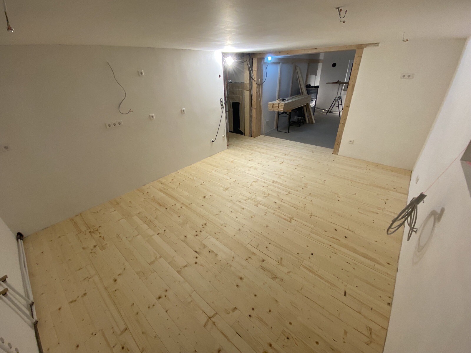 Heller Renovierungsraum mit Holzboden, offenen Kabeln und Arbeitsbereich im Hintergrund.