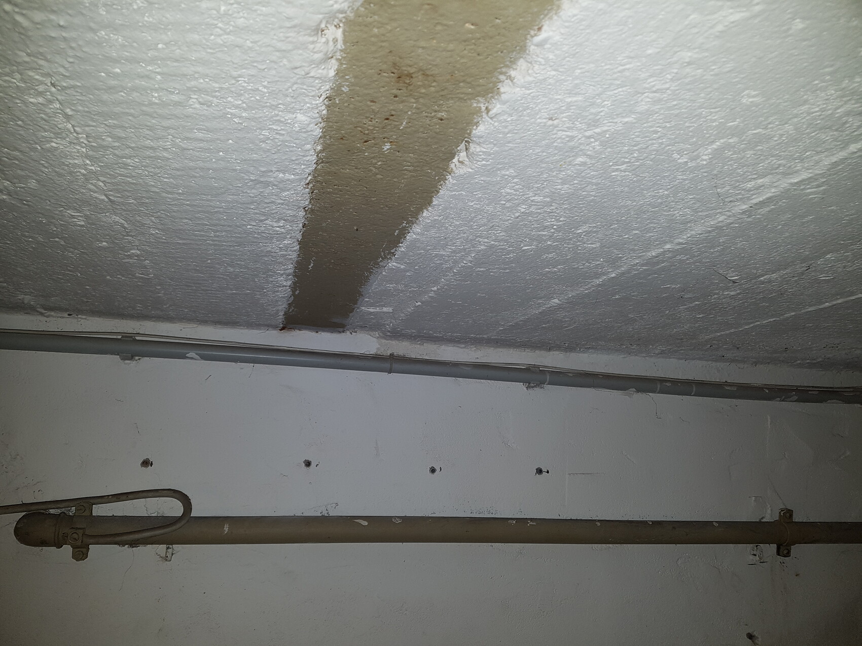 Kellerraum mit sichtbarer Rohrleitung entlang der Wand und rauer Decke