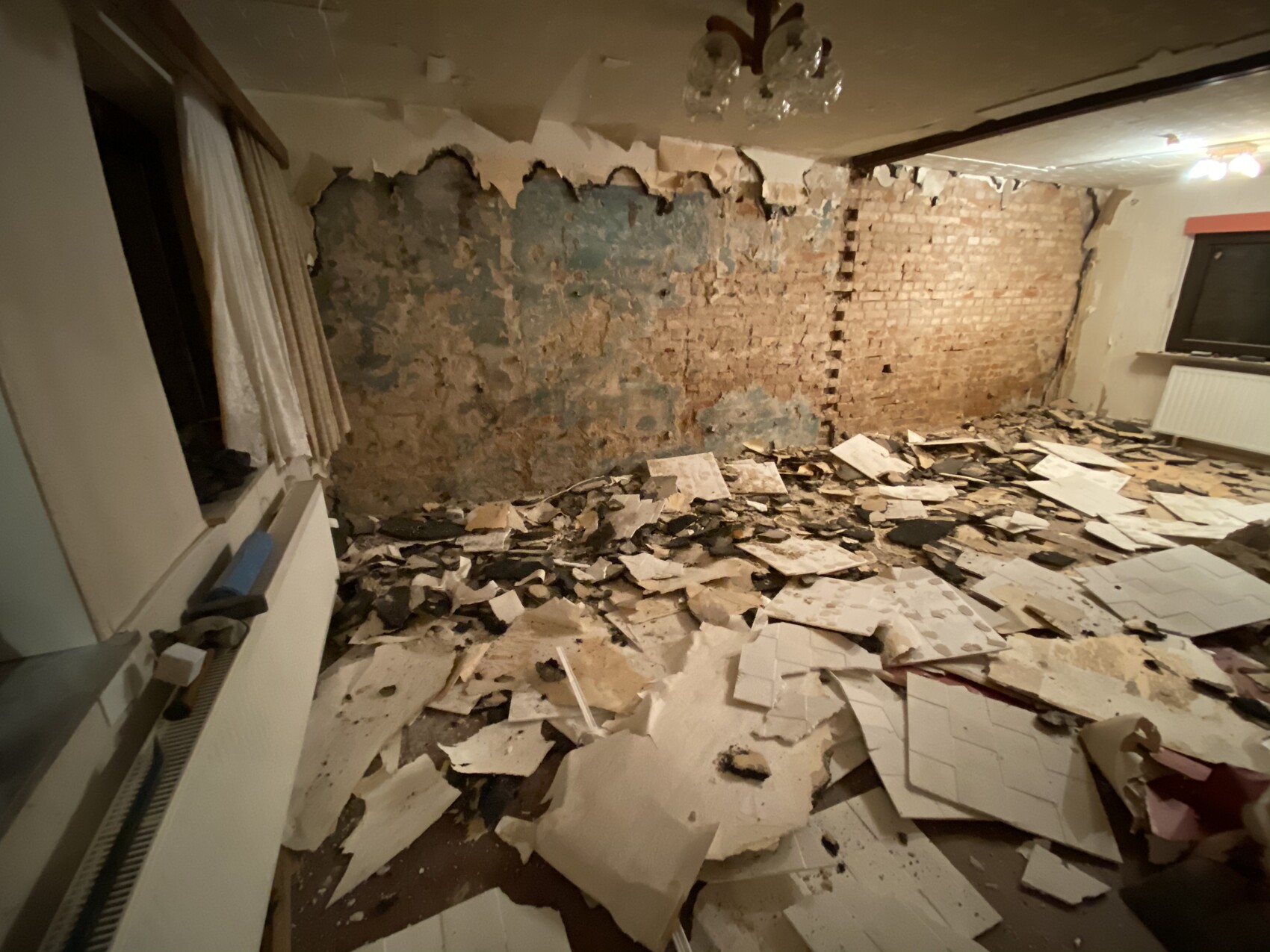 Raum in Sanierungszustand: freigelegte Backsteinwand, abplatzender Putz und Bodentrümmer.