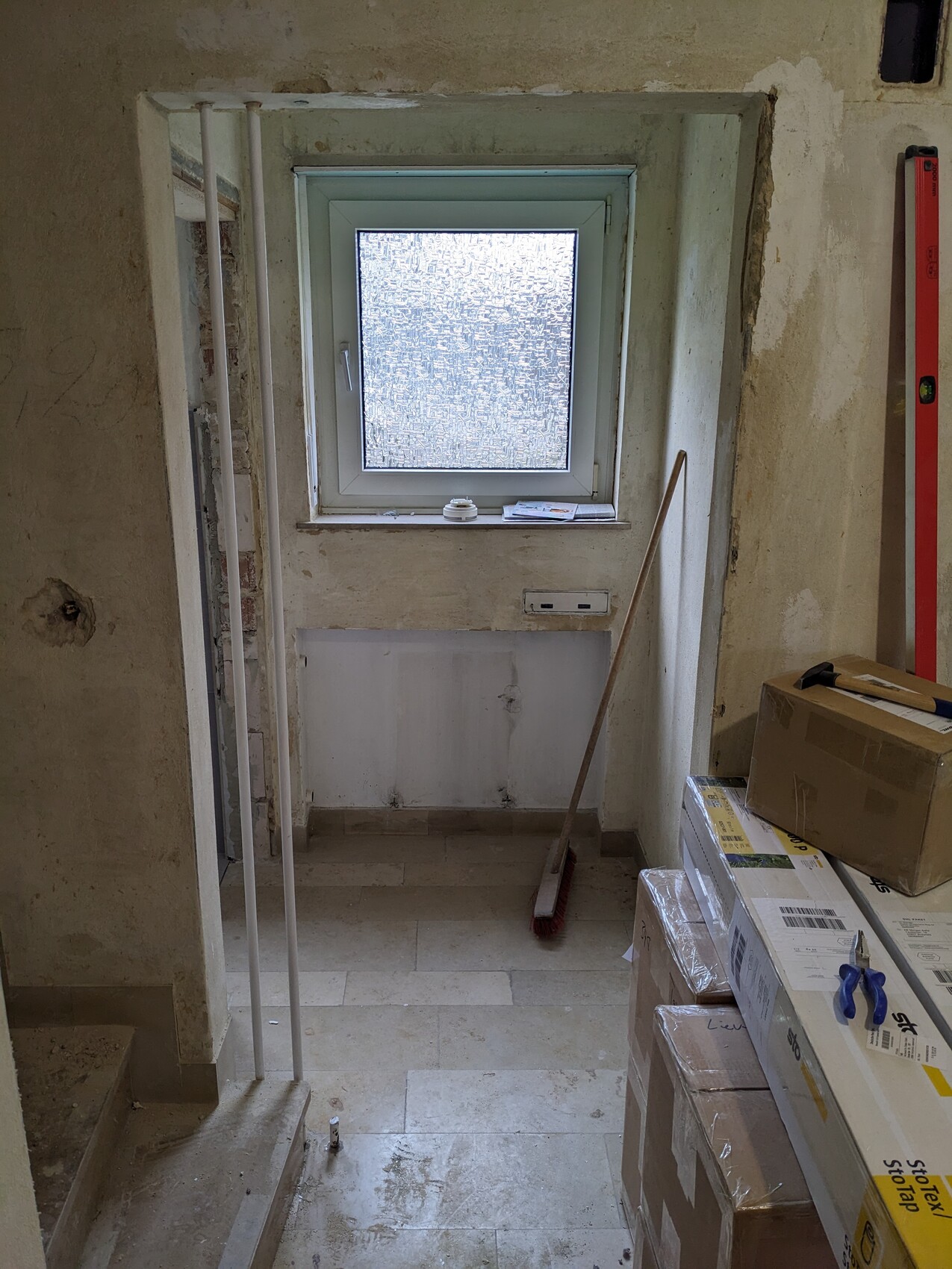 Kleiner Renovierungsraum mit Fenster, Besen, Kartons und Bauwerkzeugen.