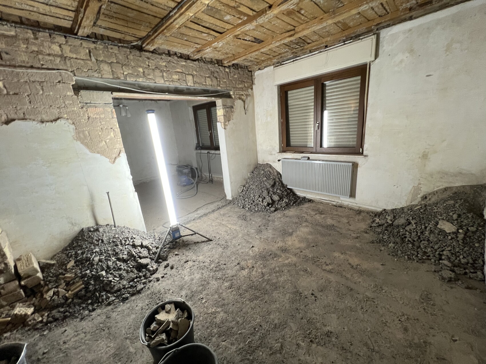 Rohbauraum mit Bauleuchte, Putz- und Steinreste, Fenster mit Heizkörper darunter.
