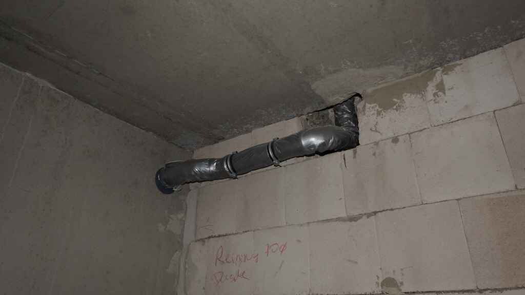 Betonwand im Keller mit installierter Rohrleitung an der Decke