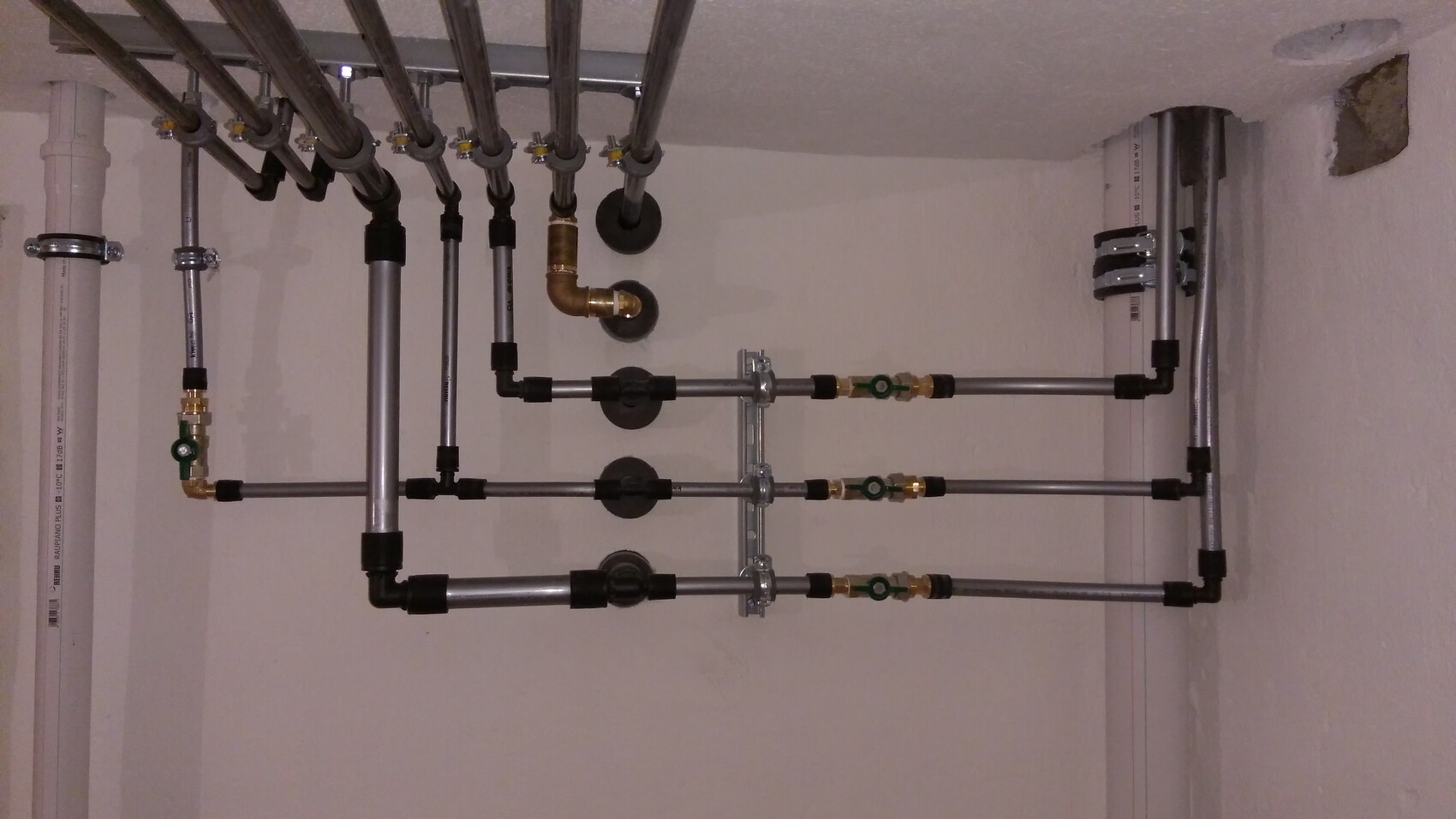 Verrohrte Wasserverteilung: Mehrere Stahlrohre mit Absperrventilen an Kellerwand.