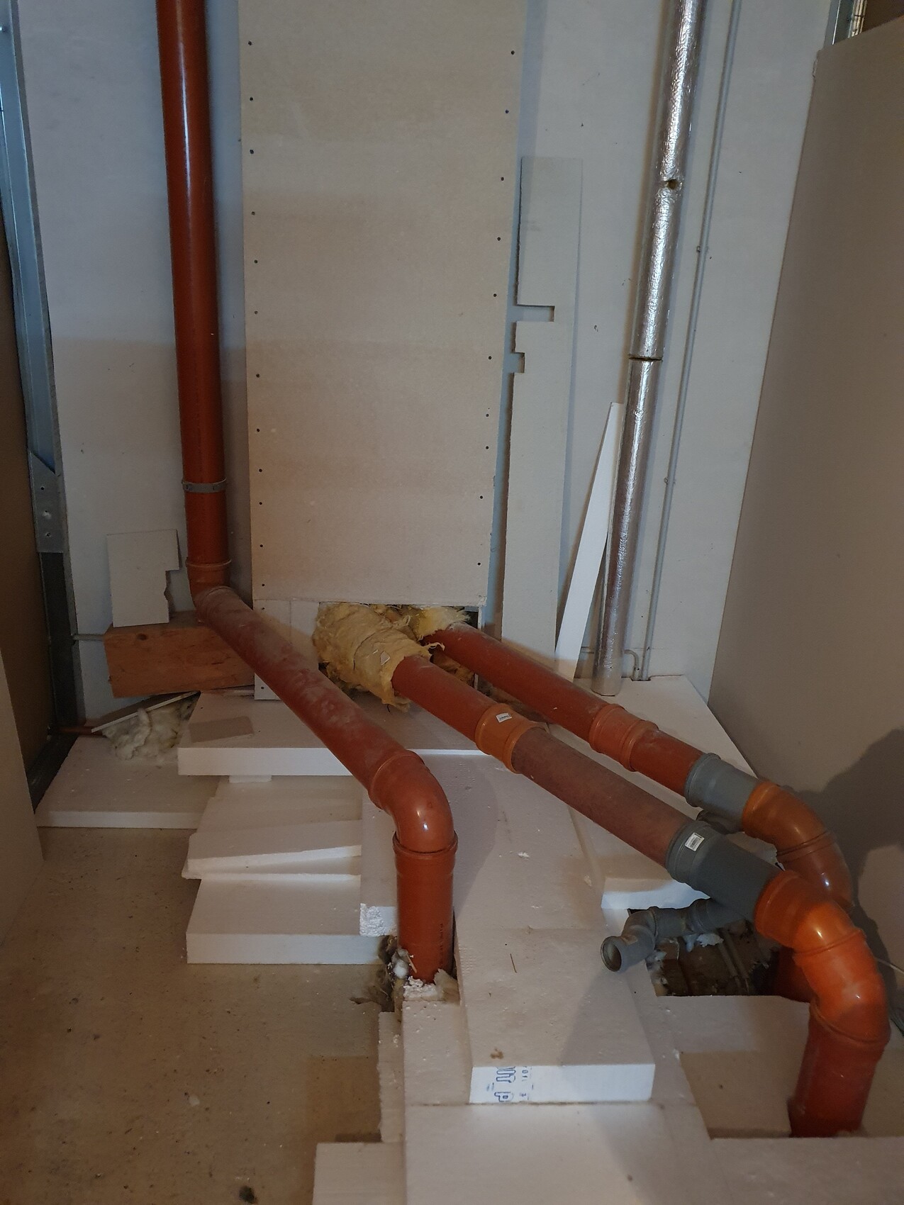 Rote Kunststoffrohre verlaufen durch einen Kellerbereich mit Dämmung und Baustellenelementen.
