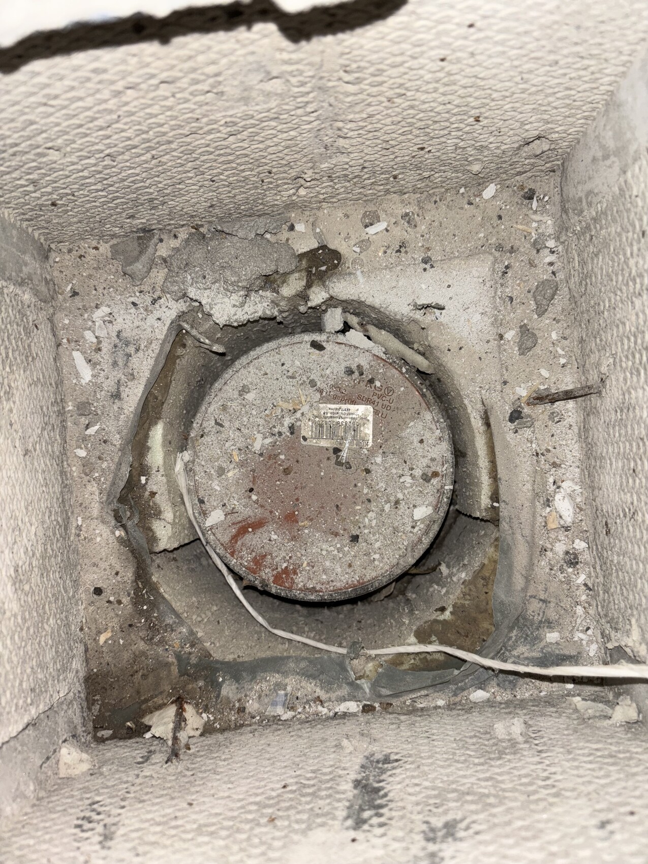 Runde Metallabdeckung in staubiger Bauöffnung, von Putz umgeben; Kabel liegt davor.