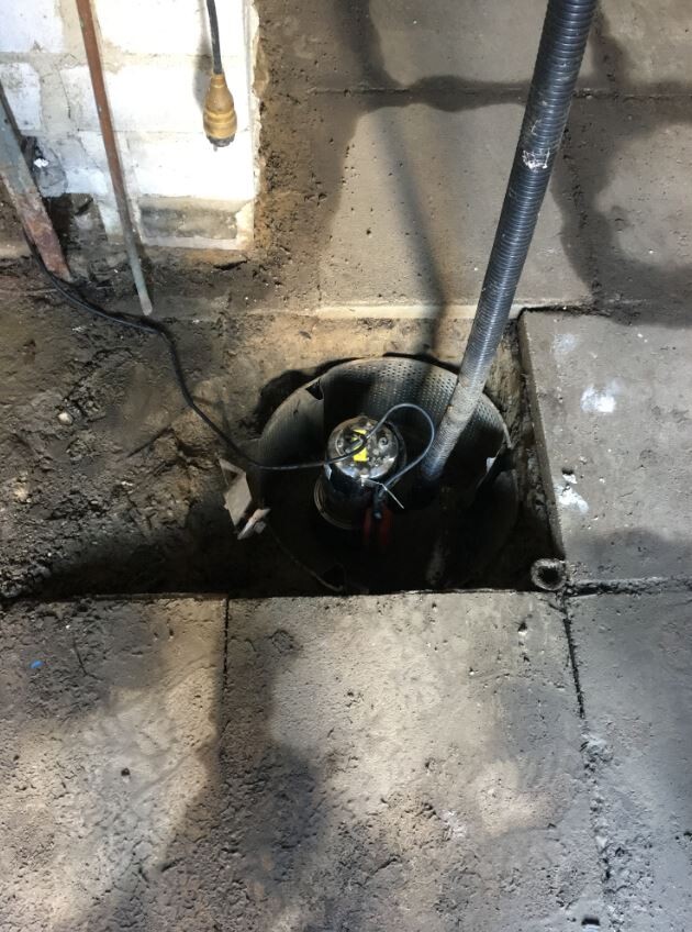 Offener Bodenschacht im Betonboden mit Sumpfpumpe, Kabeln und flexiblem Schlauch