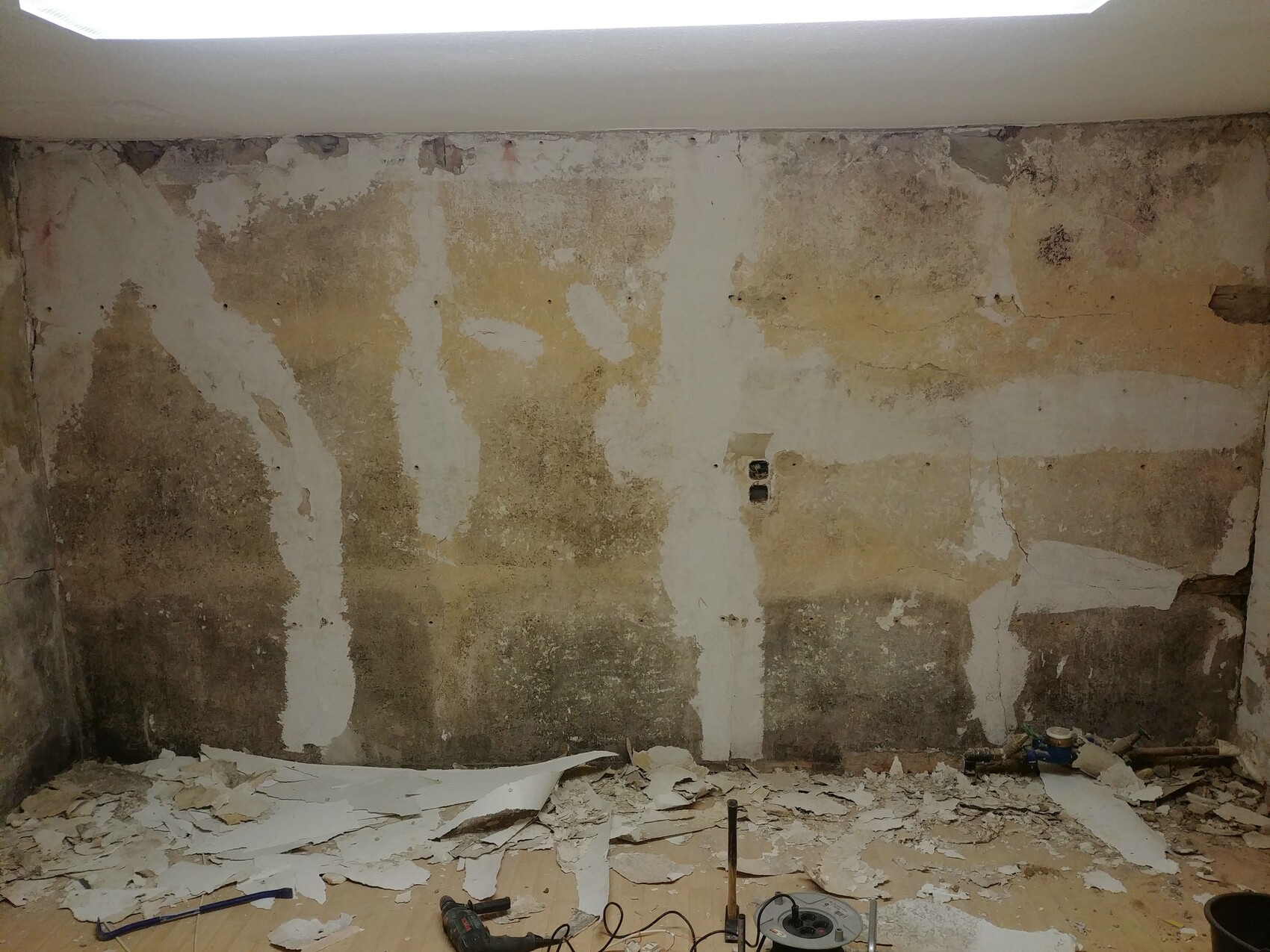 Beschädigte Kellerwand mit abblätterndem Putz, Schutt und Baustellengeräten am Boden