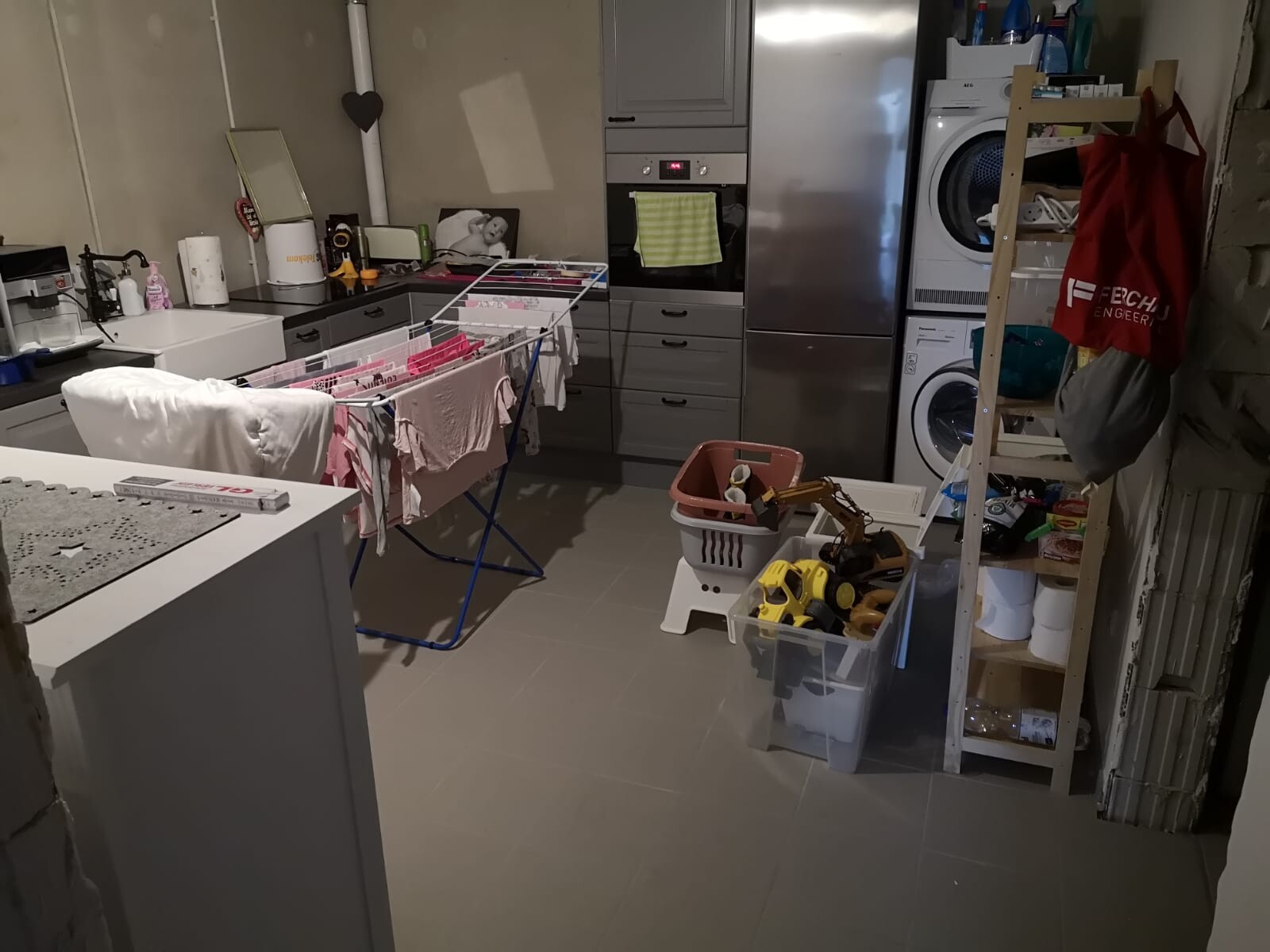 Keller-Waschküche mit Wäscheständer, Kleidung, Waschmaschine, Trockner, Regalen und Kisten.