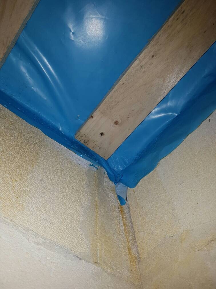 Kellerwand-Ecke mit blauer Dichtungsbahn und Feuchtigkeitsspuren an Wand und Decke.