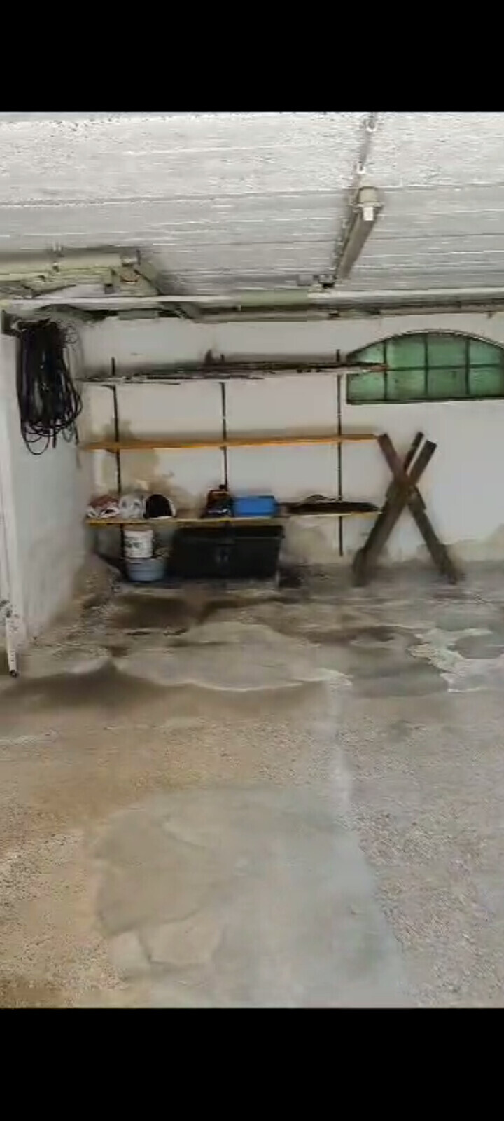 Keller-Werkstatt: nasser Boden, Wandregale mit Werkzeugen, eine Holzkreuzstütze steht daneben.