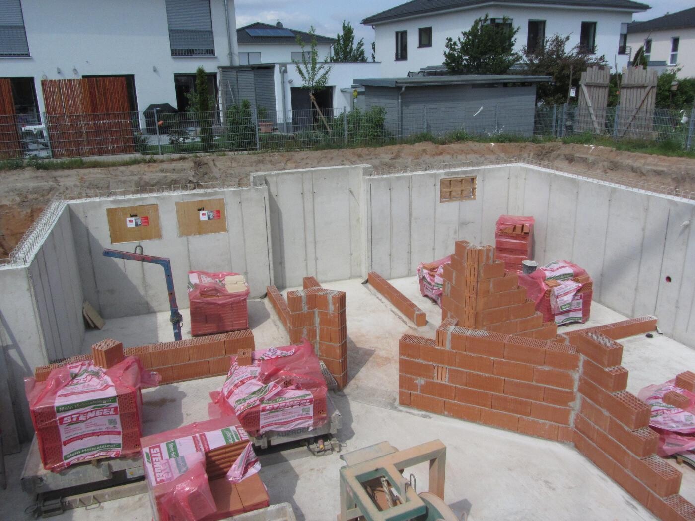 Kellerbaustelle mit unfertigen roten Ziegelwänden, Betonboden und Baustoffen in Säcken.