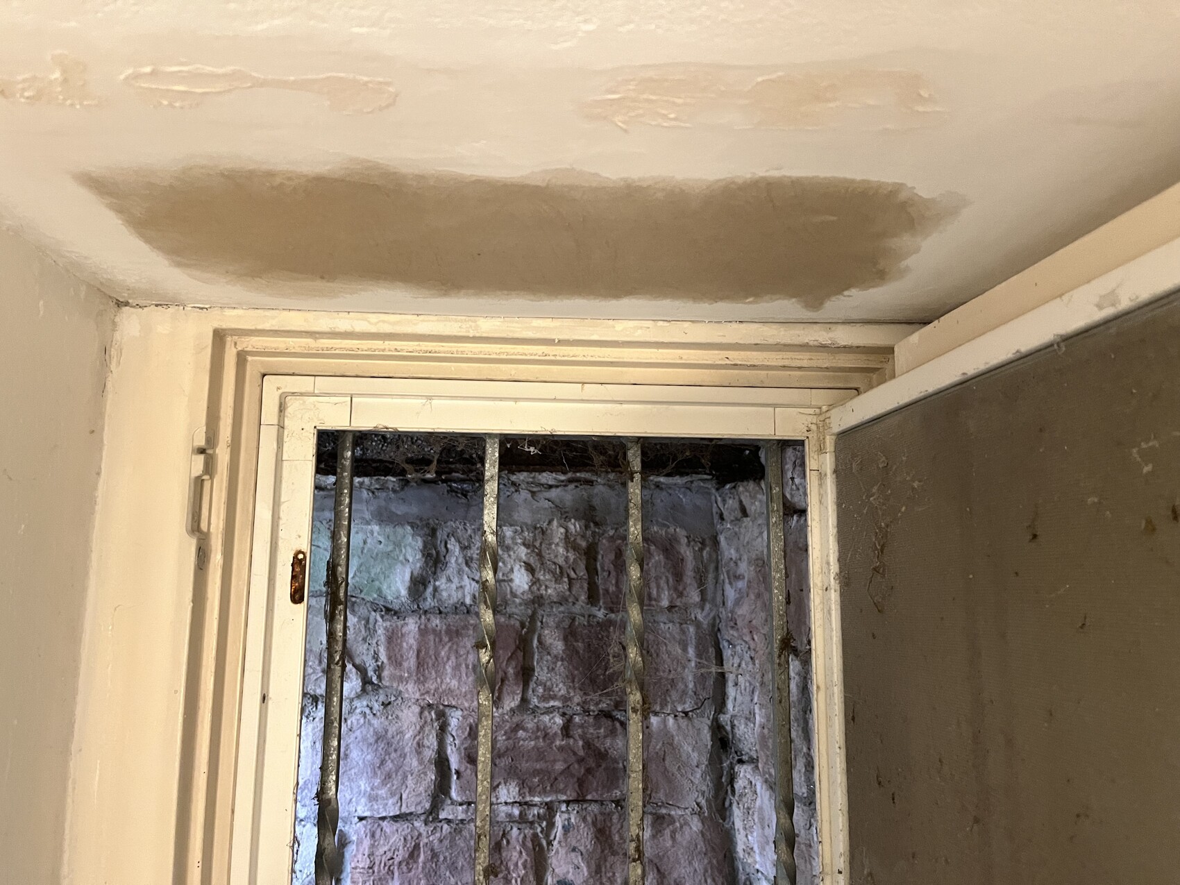 Kleines Fenster mit Metallstäben, Blick auf Steinmauer außen; Innenraum mit abblätternder Decke.