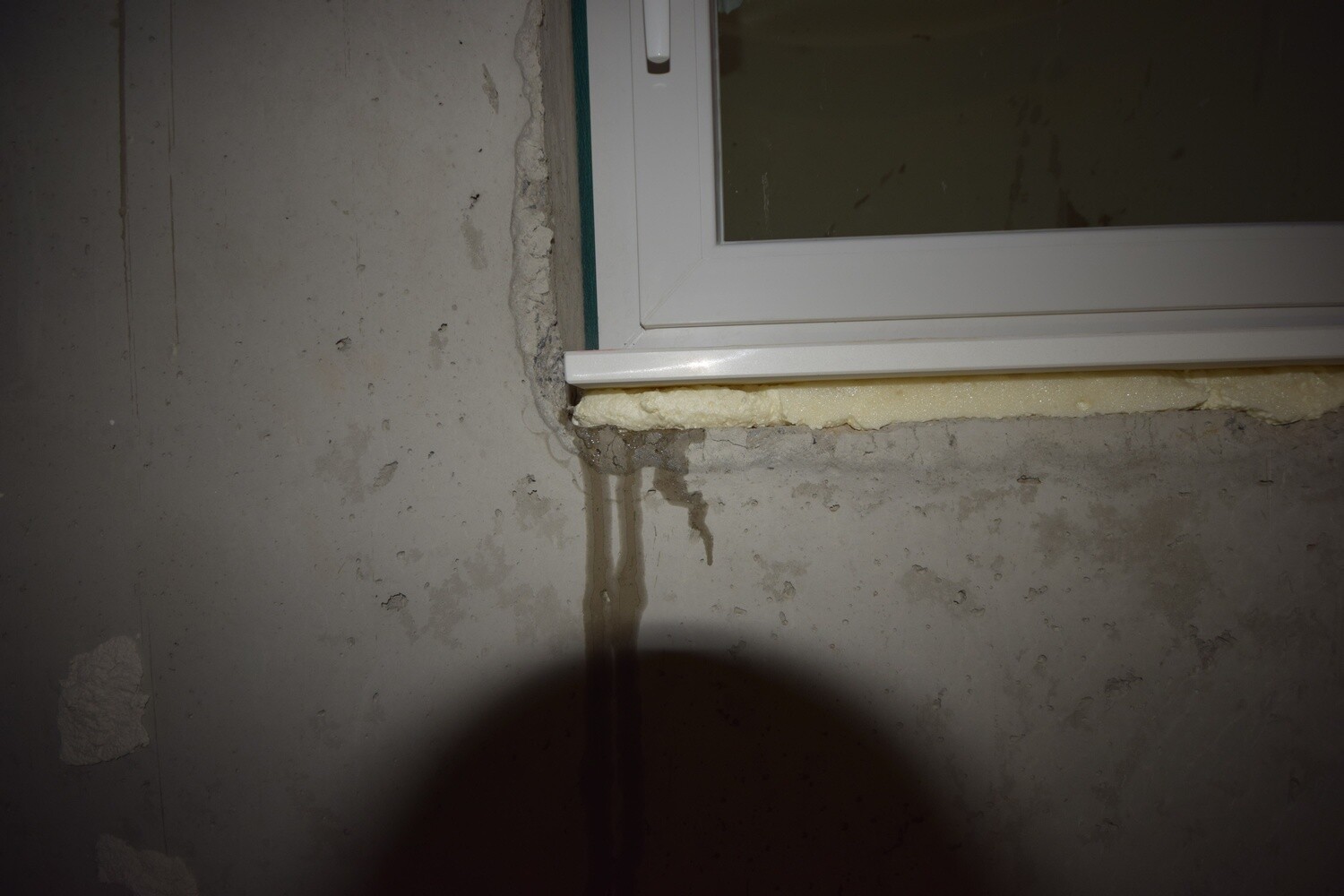 Kellerfenster in feuchter Betonwand, sichtbare Feuchtigkeit und unvollständige Dämmung