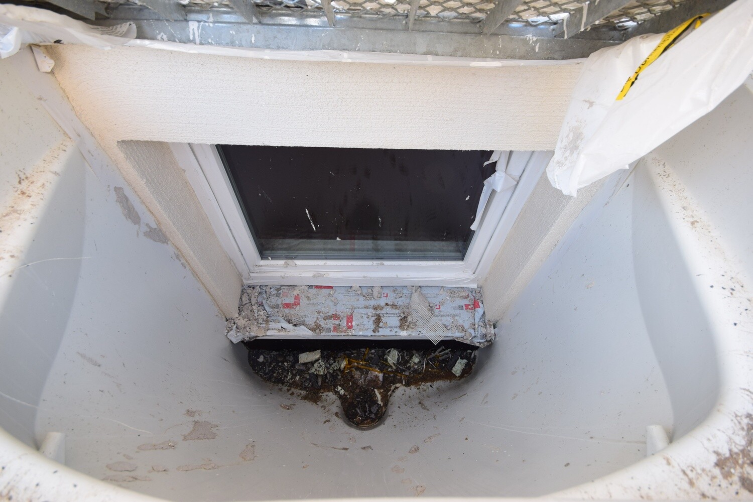 Kellerfenster in einem Fensterbrunnenbereich mit Baustellenstaub und Abbruchresten