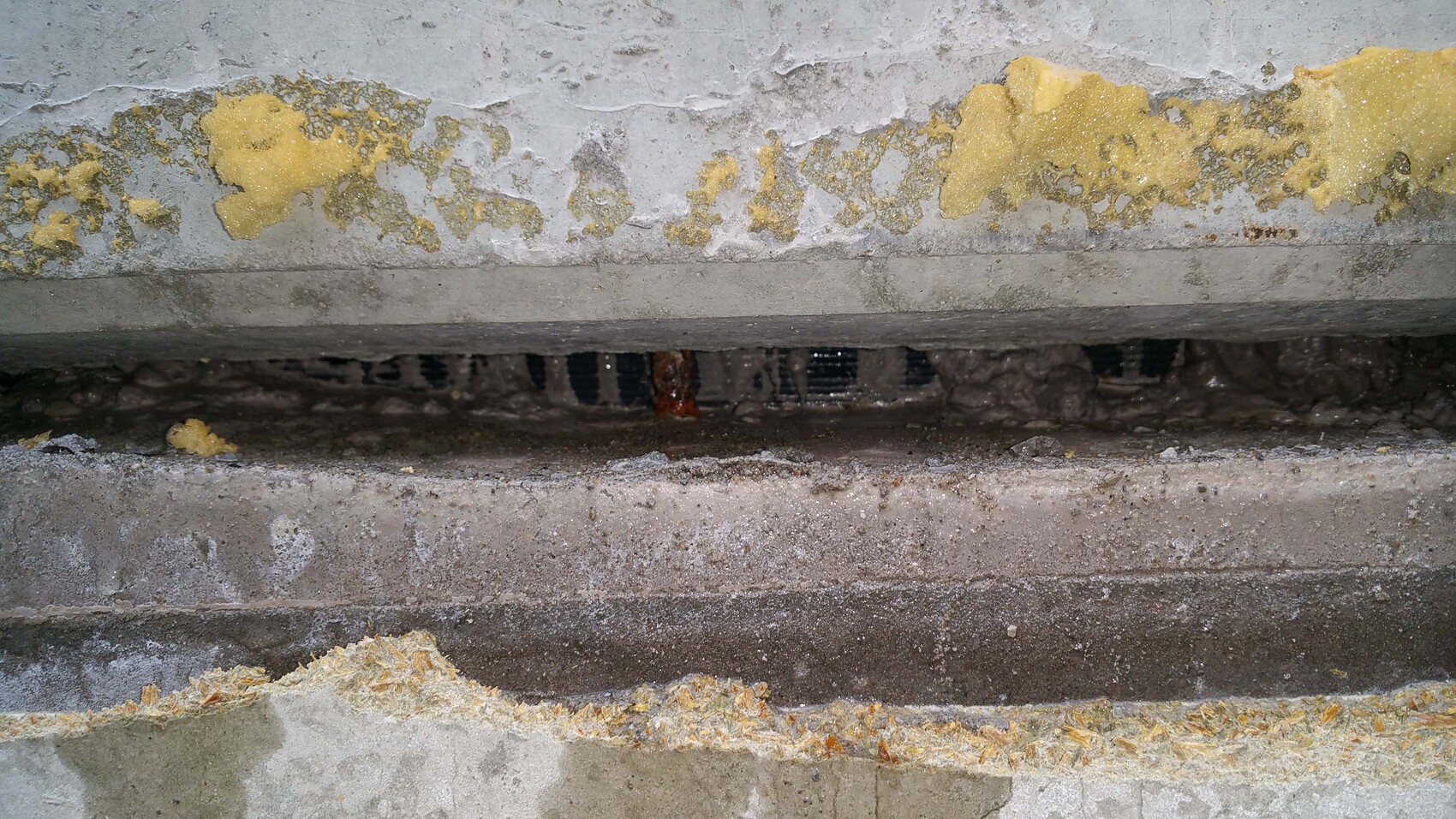 Kellerwand mit abgeplatztem Putz und gelber Dämmung sichtbar