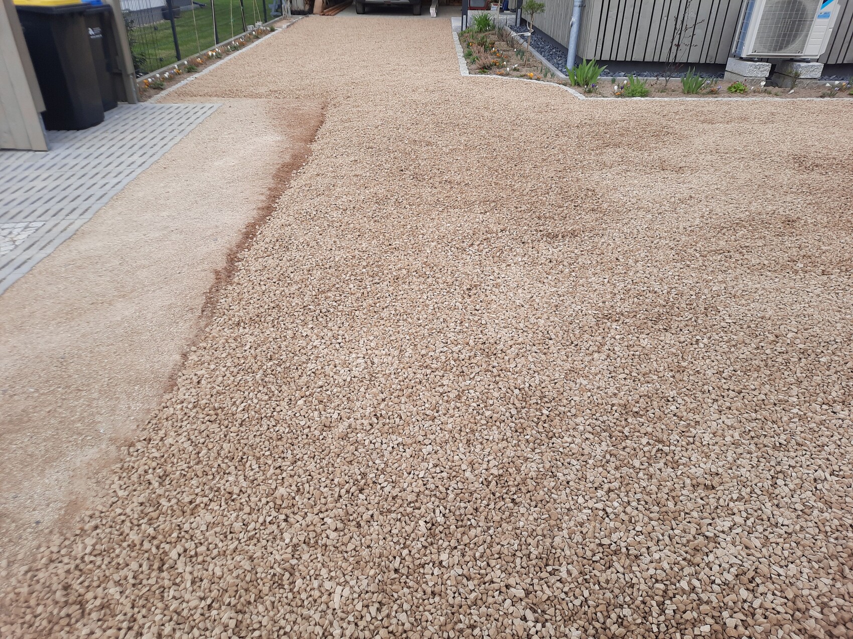 Kiesweg aus kleinen braunen Steinen neben einem Betonpfad; führt zum Haus und zur Garage, Rand mit Pflanzen.