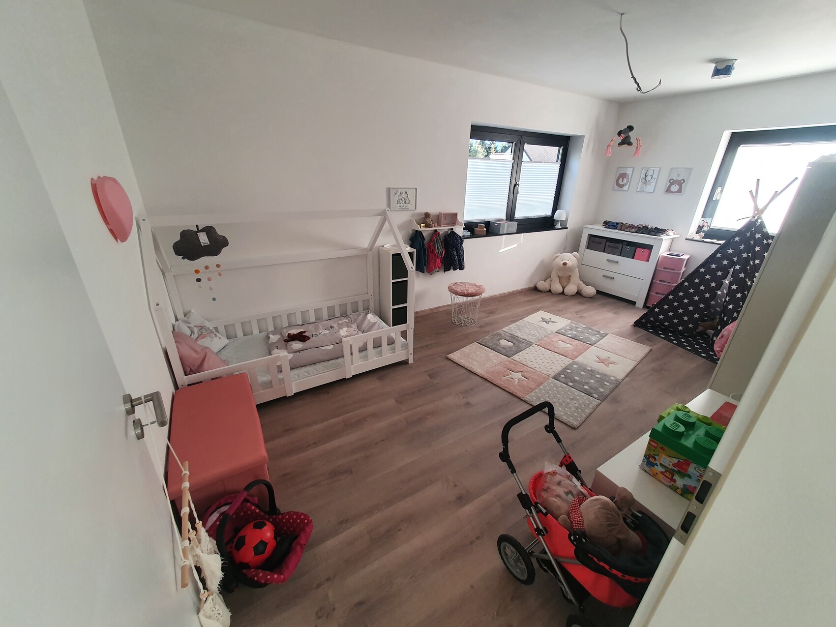 Helles Kinderzimmer mit Kleinkindbett, Teepee-Zelt, Spielteppich und Spielzeug.