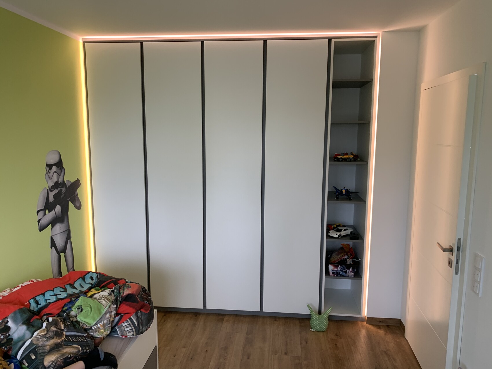 Kinderzimmer: Stormtrooper-Wandaufkleber, LED-Licht am Schrank Regal mit Spielzeugautos, buntes Bett.